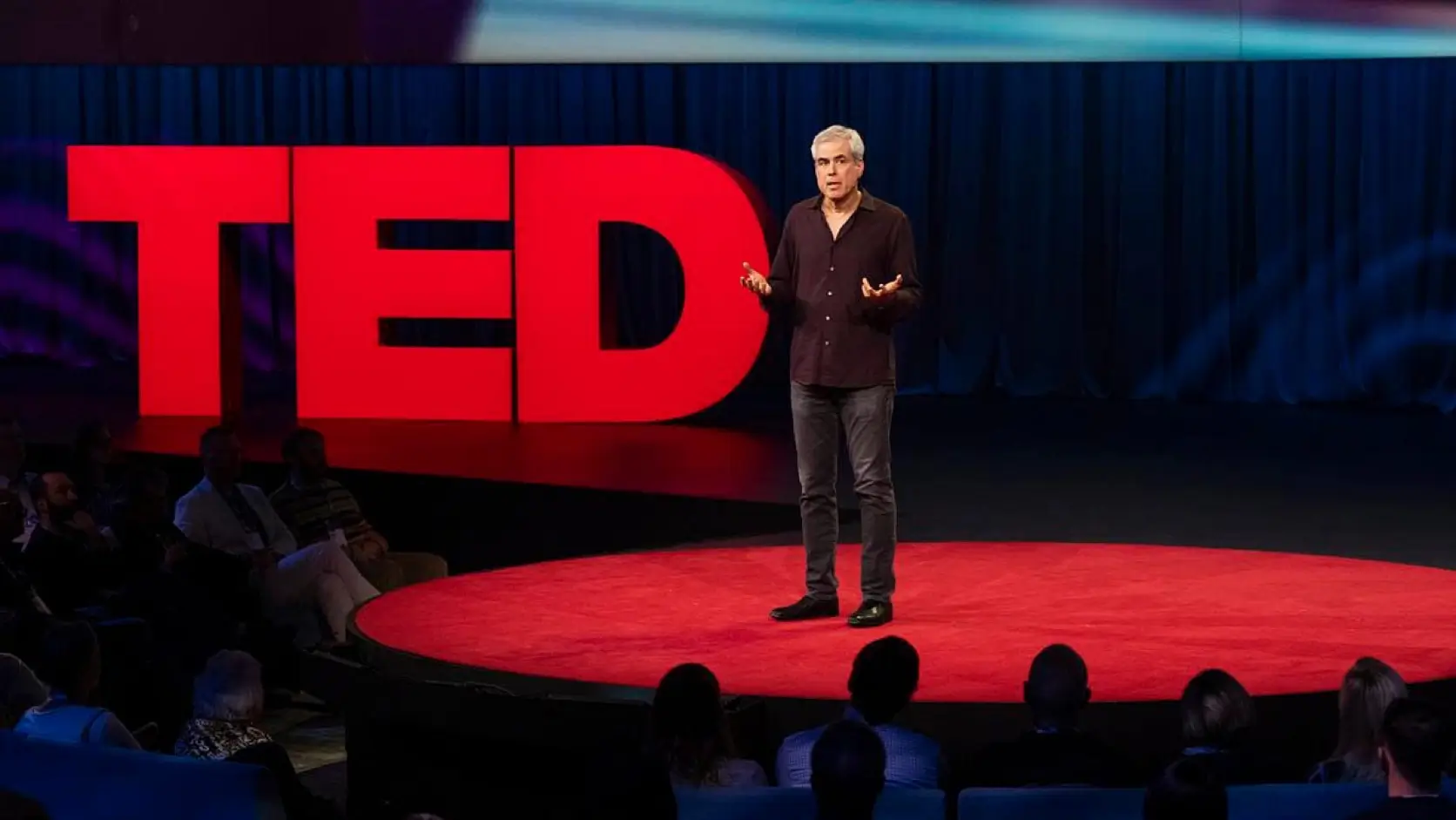 Speaker presenting on a red TED stage before a live audience
