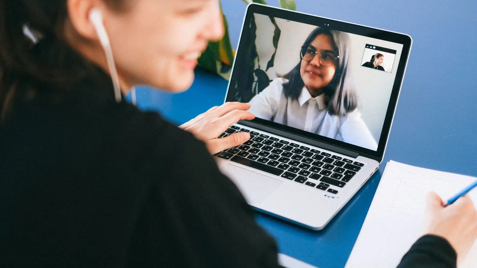Person taking notes during a remote video meeting on a laptop